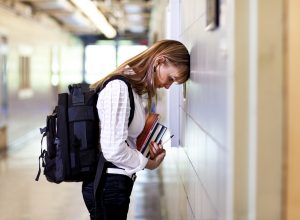 Young woman student under stress at school, thinking about her problems with her head to the wall.